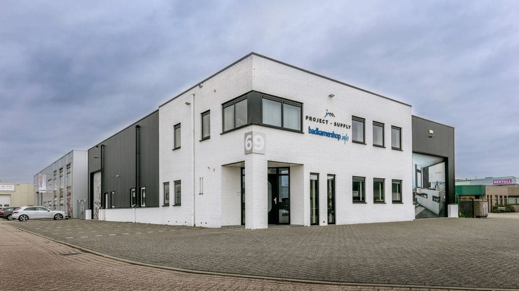 Moderne showroom van Badkamershop met wit en grijs exterieur, toonbeelden van luxe badkamers en sanitair, gevestigd op een bedrijventerrein, ideaal voor badkamer renovatie en design.